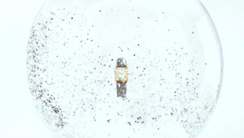 A luxurious timepiece enveloped in a swirl of glittering specks, encapsulated within a glass sphere, evoking a sense of timeless elegance amidst a snowglobe-like fantasy.