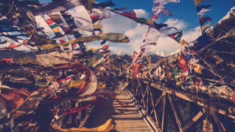 Pont en bois décoré de drapeaux de prière colorés sous un ciel bleu