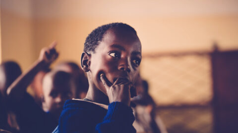 A young student in contemplation, surrounded by peers in a classroom setting.