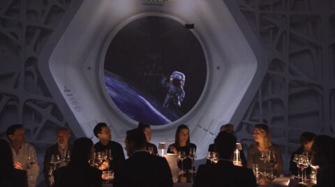 Un dîner élégant dans un lieu sur le thème de l'espace, avec une vue fascinante de la terre à travers une grande fenêtre circulaire et la silhouette d'un astronaute flottant à l'extérieur, dans un silo immersif avec un design sonore multicanal.