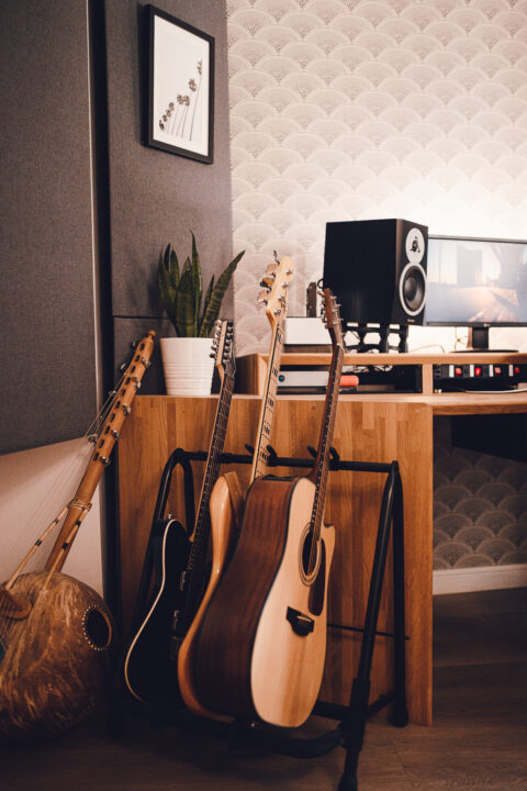A cozy music corner featuring a collection of stringed instruments next to a modern workstation with a computer and speakers, all set against an elegant textured wall and a warm, ambient-lit interior.