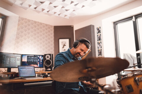 A musician immersed in his craft, drumming in a soundproof recording studio equipped with professional audio equipment.