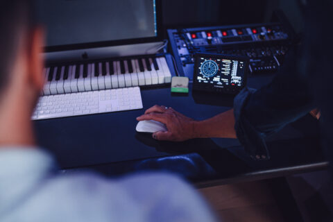 A sound designer working on music production with a midi keyboard and audio interface, illuminated by the cool glow of screen and led lights.