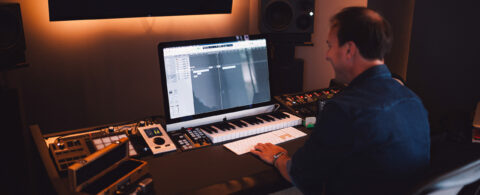 Un sound designer en plein montage de pistes sur un ordinateur dans un studio de mixage, entouré d'équipements audio professionnels.