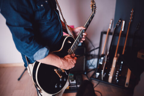 Homme jouant de la guitare électrique noire dans un studio avec plusieurs guitares en arrière-plan.