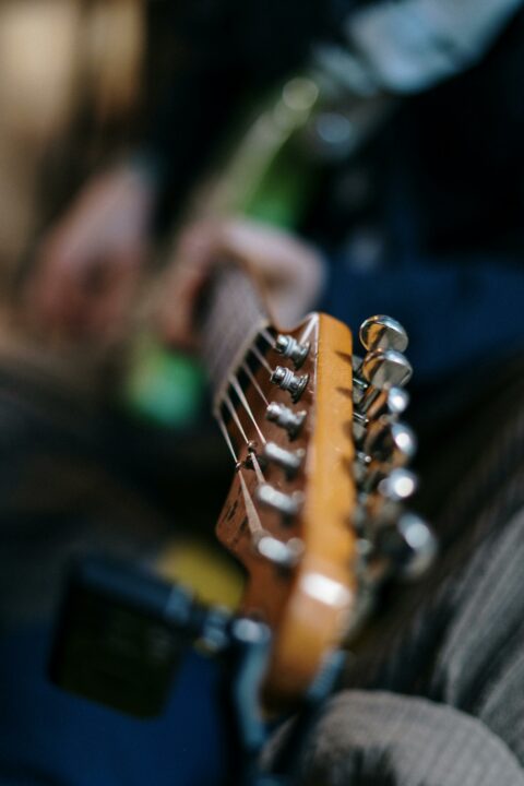 A detailed view of a guitar's headstock, focusing on the metallic tuning pegs with a blurred background