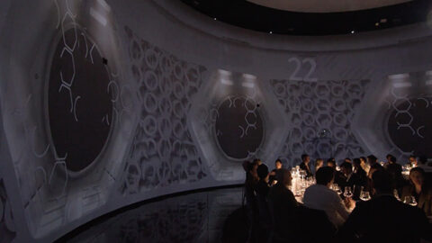 An immersive dining experience where guests enjoy their meal surrounded by multicanal sound design and elegant, dimly-lit wall projections in a curved, modern space.