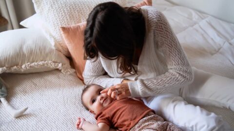 Mère habillée en blanc prenant soin de son bébé couché sur un lit.