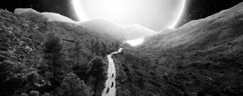 Chemin serpentant à travers un paysage montagneux sous une énorme lune blanche, en noir et blanc.
