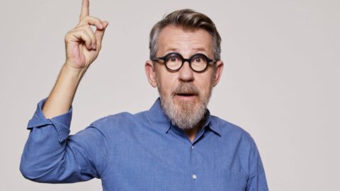Jamy Gourmaud avec lunettes rondes et chemise bleue, levant un doigt en l'air, l'air étonné