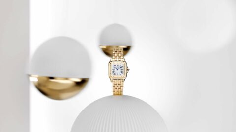 Montre dorée élégante affichée sur un fond blanc épuré avec des formes sphériques.